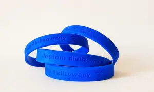 Niebieska opaska na ręce z napisem "Jestem dializowany" i logo Fresenius Medical Care.