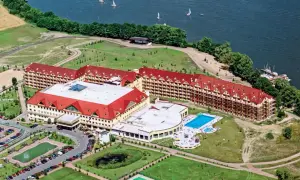 Widok z lotu ptaka na rozległy kompleks hotelowy z czerwonymi dachami, basenem i jeziorem. Czy to pierwszy hotel Gołębiowski?
