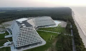Nowoczesny hotel o tarasowej architekturze nad brzegiem morza, otoczony lasem.