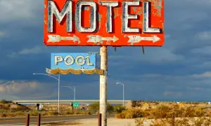 Stary, zniszczony neonowy szyld "MOTEL" i "POOL" na tle burzowego nieba. Obok droga i most.