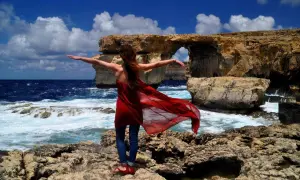 Kobieta w czerwonej sukience na Malcie, przy Azure Window. Idealne miejsce, by poczuć wiosnę, gdy zastanawiasz się, gdzie cieplej w kwietniu Cypr czy Malta.