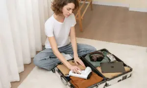 Kobieta pakuje walizkę, w której widać ubrania, słuchawki, aparat i tablet.