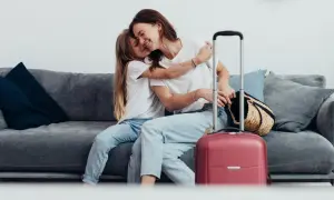 Mama i córka przytulają się na kanapie obok walizki. Wszyscy, którzy chcą podróżować, mogą zameldować się w hotelu.