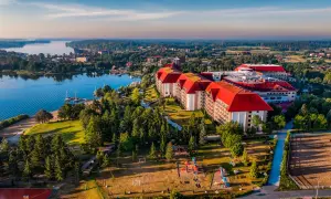 Hotel Gołębiewski w Mikołajkach, z czerwonymi dachami, otoczony zielenią i jeziorem, wygląda jak miejsce z bajki.