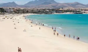 Słoneczna plaża z turystami, turkusowe morze i góry w tle. Czy lot na Wyspy Kanaryjskie jest bezpieczny? Tak, to popularny i bezpieczny kierunek wakacyjny.