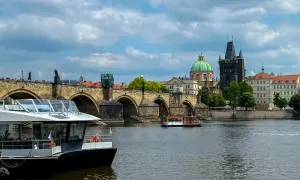 Widok na Most Karola w Pradze, z łodziami na Wełtawie. Turyści zastanawiają się, czy w Pradze można płacić euro, ale czeska korona jest walutą.