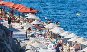 Ludzie odpoczywają na plaży pod parasolami, w tle widać turkusowe morze.