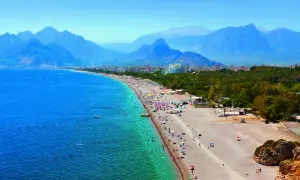 Tłum ludzi na plaży w Antalyi, z górami w tle. Czy Antalya jest bezpieczna? Wygląda na to, że turyści cieszą się słońcem i morzem.