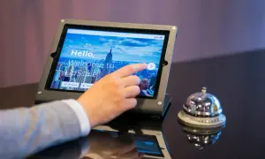 Dłoń dotyka ekranu tabletu z napisem "Welcome to UpScale". Czy to oznacza, że ile trzeba mieć lat żeby zameldować się w hotelu?