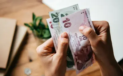 Ręce trzymają banknoty 10 i 20 lir tureckich. Planujesz podróż i zastanawiasz się, jaką walutę zabrać do Turcji? Lira turecka to odpowiedź!