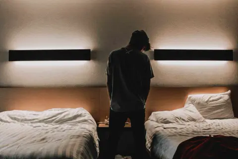 Młody mężczyzna stoi w pokoju hotelowym z dwoma łóżkami. Czy osoba niepełnoletnia może zameldować się w hotelu?