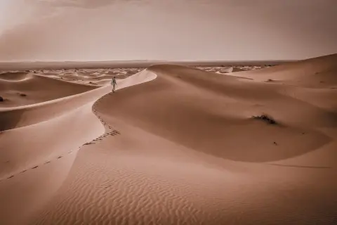 Samotna postać wędruje po piaszczystych wydmach. Czy Tunezja jest teraz bezpieczna? Pustynny krajobraz sugeruje spokój i ciszę.