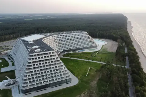 Nowoczesny hotel o tarasowej architekturze nad brzegiem morza, otoczony lasem.