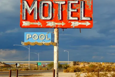 Stary, zniszczony neonowy szyld "MOTEL" i "POOL" na tle burzowego nieba. Obok droga i most.