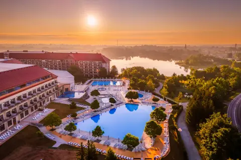 Hotel Gołębiewski w Mikołajkach, z basenami i jeziorem w tle, o wschodzie słońca. Ile lat ma hotel Gołębiewski w Mikołajkach?