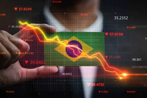 Ręka trzyma flagę Brazylii na tle wykresu finansowego. Kiedyś waluta Brazylii, real, doświadcza spadków.