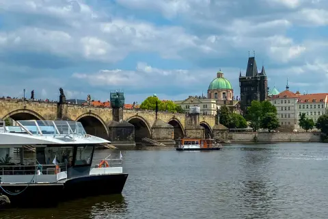 Widok na Most Karola w Pradze, z łodziami na Wełtawie. Turyści zastanawiają się, czy w Pradze można płacić euro, ale czeska korona jest walutą.