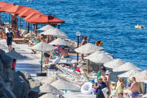 Ludzie odpoczywają na plaży pod parasolami, w tle widać turkusowe morze.