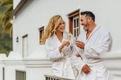 Para, która cieszy się szampanem na balkonie w hotelowych szatach. Zastanawiasz się, ile kosztuje doba hotelowa w takim miejscu?