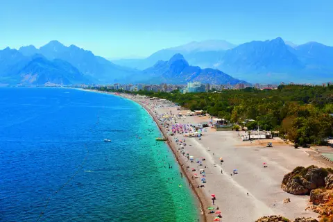 Tłum ludzi na plaży w Antalyi, z górami w tle. Czy Antalya jest bezpieczna? Wygląda na to, że turyści cieszą się słońcem i morzem.