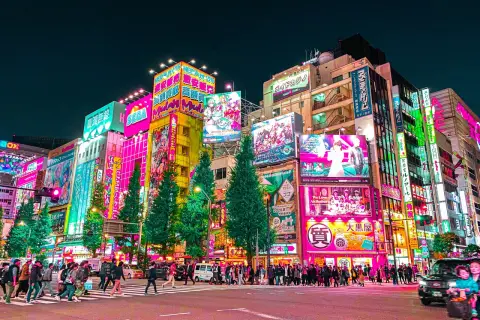 Akihabara nocą, pełna neonów i reklam, to miejsce, co warto zobaczyć w Tokio. Tłumy ludzi przechodzą przez pasy.