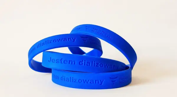 Niebieska opaska na ręce z napisem "Jestem dializowany" i logo Fresenius Medical Care.