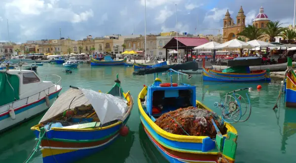 Kolorowe łodzie rybackie w porcie Marsaxlokk. Czy na Malcie jest drogo? Widok sugeruje, że życie toczy się tu spokojnie, a ceny mogą być przystępne.