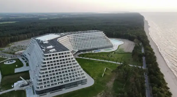 Nowoczesny hotel o tarasowej architekturze nad brzegiem morza, otoczony lasem.