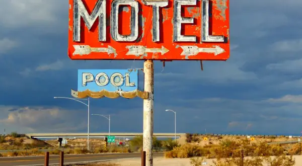 Stary, zniszczony neonowy szyld "MOTEL" i "POOL" na tle burzowego nieba. Obok droga i most.
