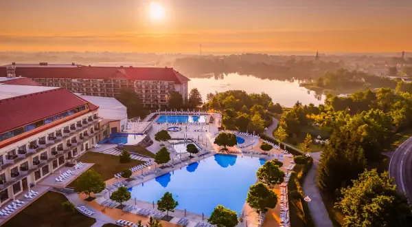 Hotel Gołębiewski w Mikołajkach, z basenami i jeziorem w tle, o wschodzie słońca. Ile lat ma hotel Gołębiewski w Mikołajkach?