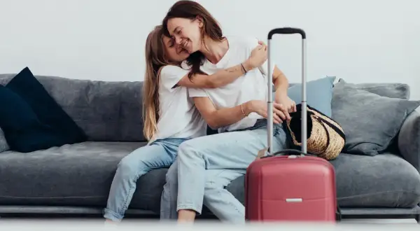 Mama i córka przytulają się na kanapie obok walizki. Wszyscy, którzy chcą podróżować, mogą zameldować się w hotelu.
