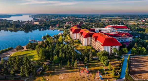 Hotel Gołębiewski w Mikołajkach, z czerwonymi dachami, otoczony zielenią i jeziorem, wygląda jak miejsce z bajki.