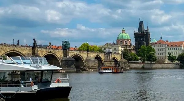 Widok na Most Karola w Pradze, z łodziami na Wełtawie. Turyści zastanawiają się, czy w Pradze można płacić euro, ale czeska korona jest walutą.