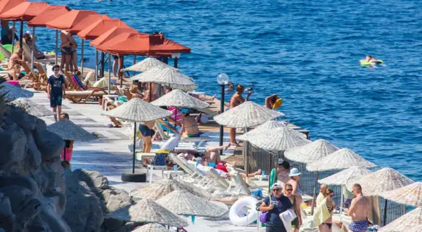 Ludzie odpoczywają na plaży pod parasolami, w tle widać turkusowe morze.