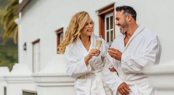Para, która cieszy się szampanem na balkonie w hotelowych szatach. Zastanawiasz się, ile kosztuje doba hotelowa w takim miejscu?