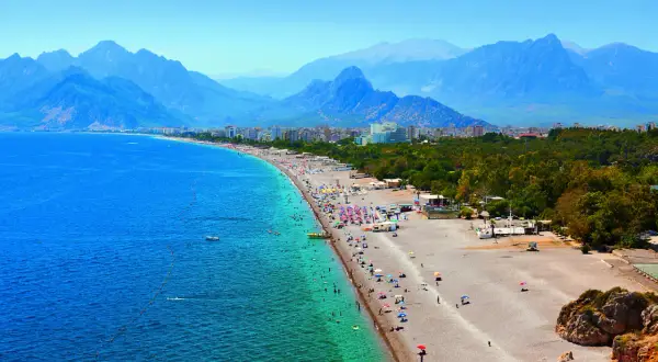 Tłum ludzi na plaży w Antalyi, z górami w tle. Czy Antalya jest bezpieczna? Wygląda na to, że turyści cieszą się słońcem i morzem.