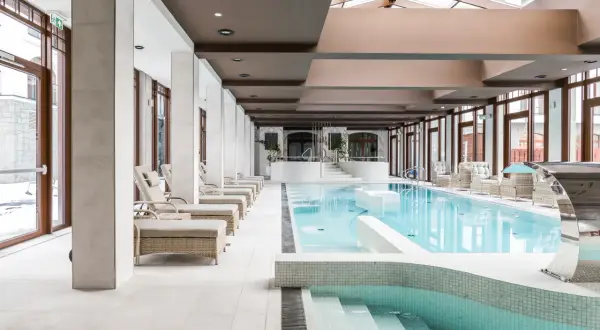 Luksusowy basen hotelowy z leżakami i jacuzzi. Zastanawiasz się, ile kosztuje jedna noc w hotelu z takim zapleczem?