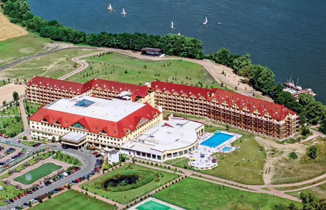 Widok z lotu ptaka na rozległy kompleks hotelowy z czerwonymi dachami, basenem i jeziorem. Czy to pierwszy hotel Gołębiowski?