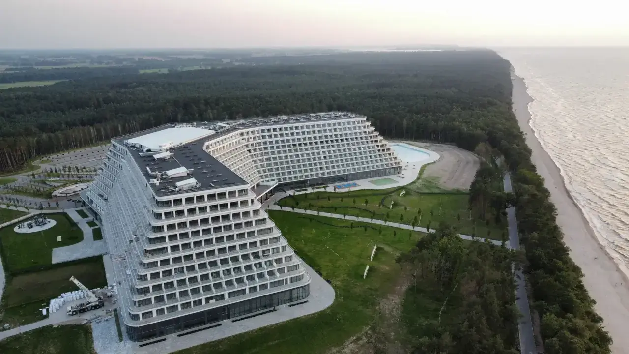 Nowoczesny hotel o tarasowej architekturze nad brzegiem morza, otoczony lasem.