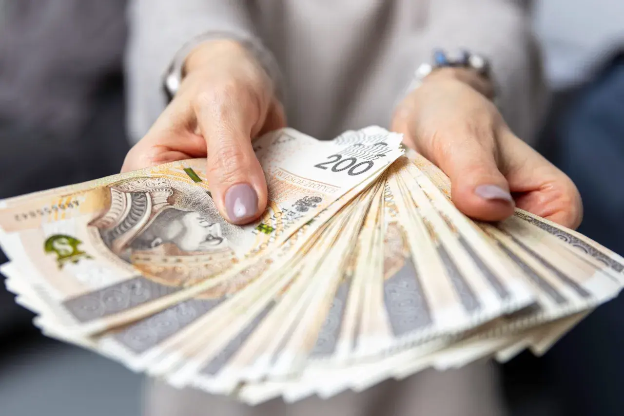 Dłonie trzymają wachlarz banknotów 200 zł. Zastanawiasz się, ile zarabia hotelarz?