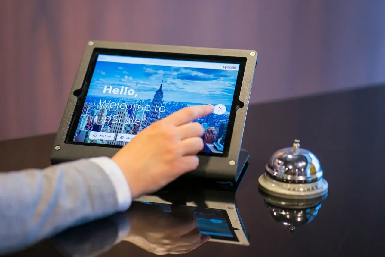 Dłoń dotyka ekranu tabletu z napisem "Welcome to UpScale". Czy to oznacza, że ile trzeba mieć lat żeby zameldować się w hotelu?