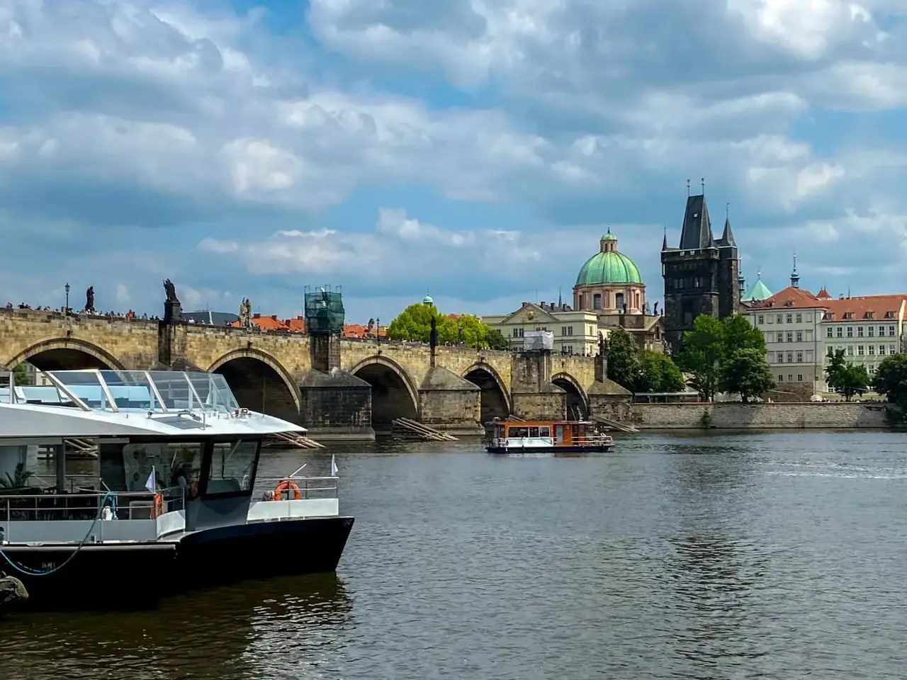 Widok na Most Karola w Pradze, z łodziami na Wełtawie. Turyści zastanawiają się, czy w Pradze można płacić euro, ale czeska korona jest walutą.