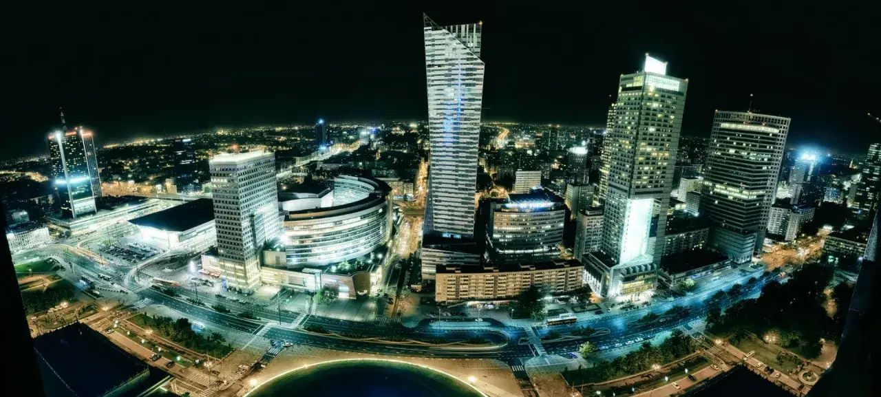 Warszawskie wieżowce nocą. Widać hotel Marriott, który ma wiele pięter, otoczony innymi budynkami i ulicami.