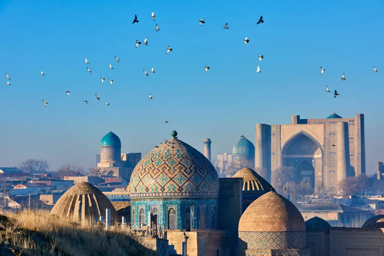 Błękitne kopuły i minarety w Uzbekistanie, nad którymi latają ptaki. Czy wyjazd do Uzbekistanu jest bezpieczny? Tak, to piękny kraj.