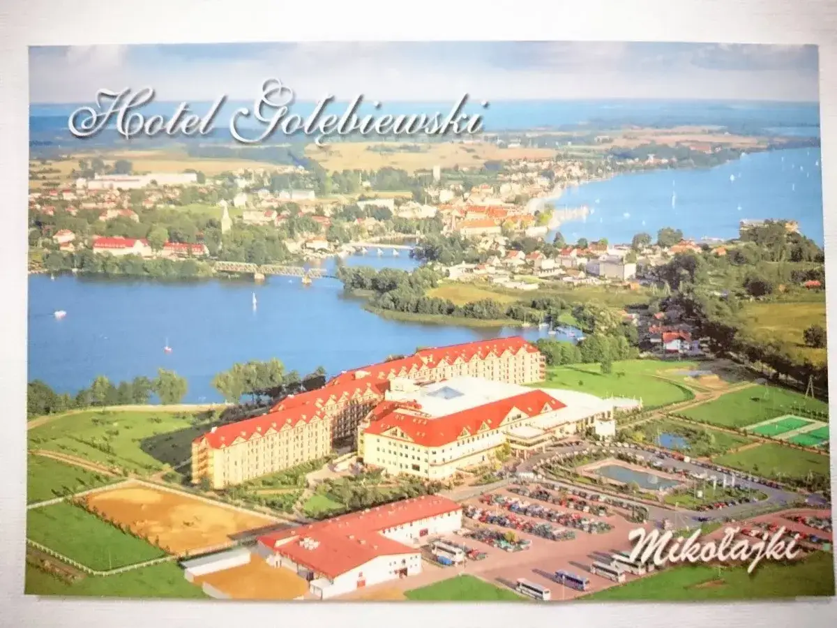Widok na Hotel Gołębiewski w Mikołajkach, który powstał w 1999 roku. Rozległy kompleks hotelowy nad jeziorem, z parkingiem i terenami zielonymi.