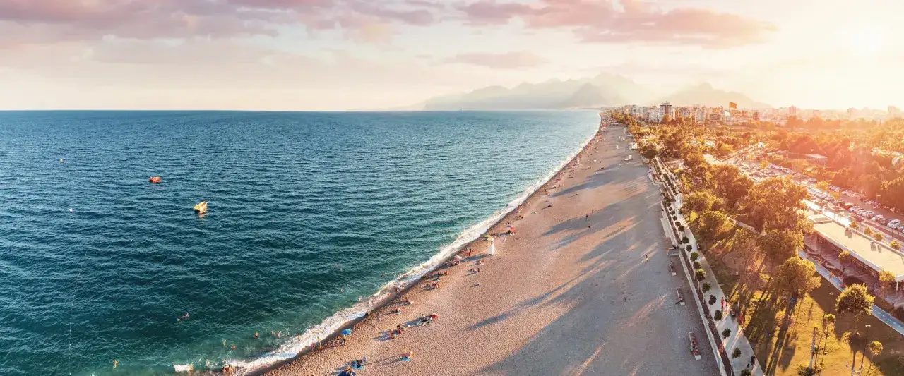 Słoneczna plaża w Antalyi, pełna ludzi odpoczywających nad morzem. Czy Antalya jest bezpieczna? Wygląda na to, że tak, bo turyści cieszą się wakacjami.