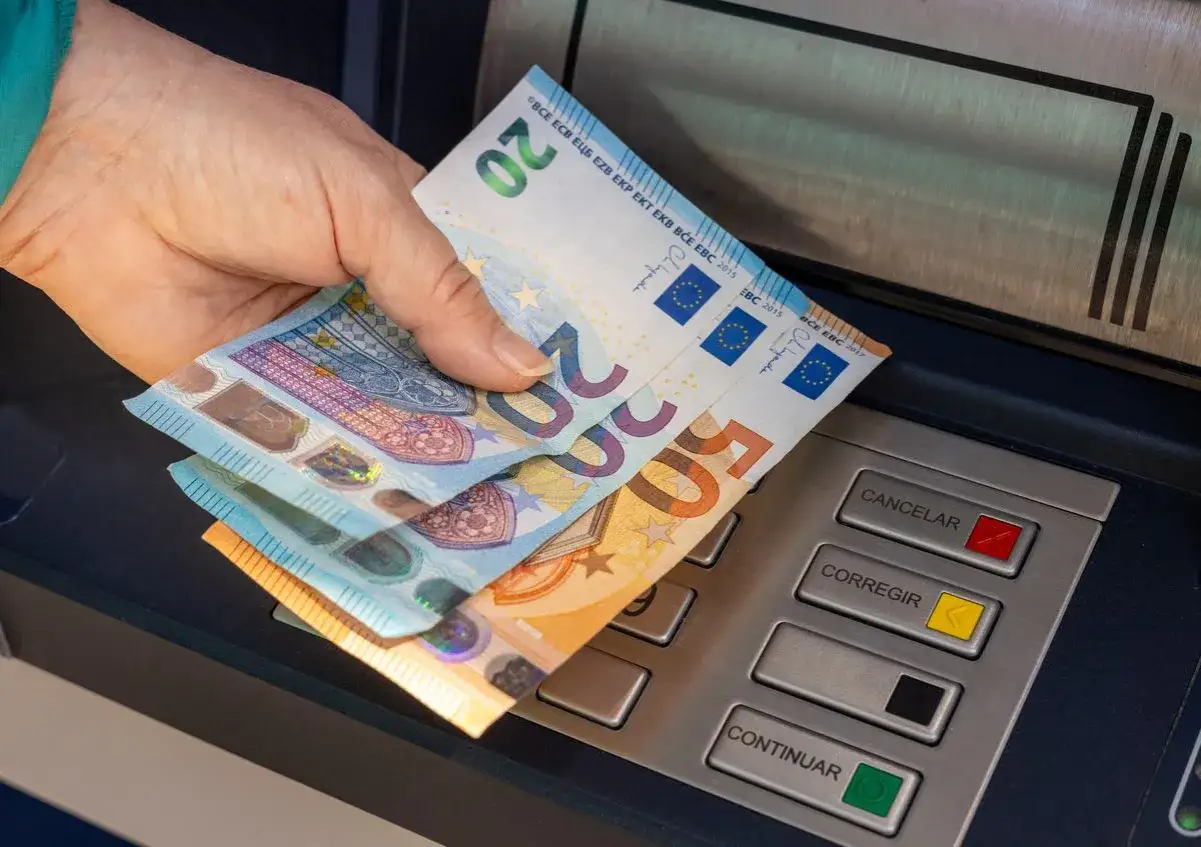 Dłoń trzyma banknoty euro przy bankomacie. W Hiszpanii płaci się właśnie euro, co widać na banknotach 20 i 50 euro.