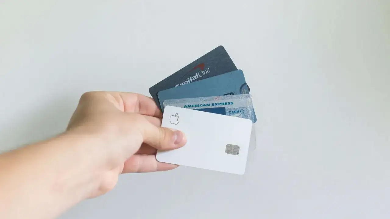 Dłoń trzyma stos kart płatniczych, w tym Apple Card i American Express. Włochy używają euro, więc te karty będą tam działać.