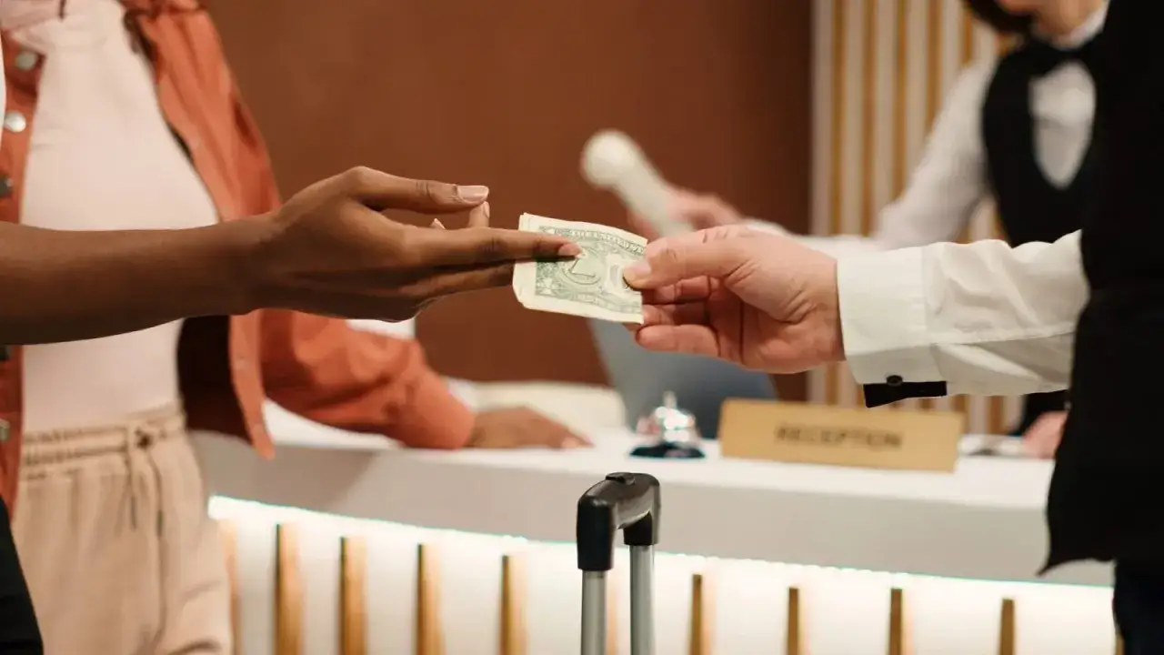 Dłoń podaje banknot pracownikowi hotelu przy recepcji. Prosty sposób, jak zostawić napiwek w hotelu.