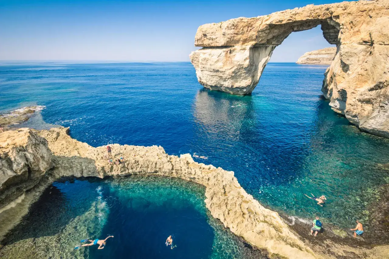 Malta: idealne miesiące na zwiedzanie i kąpiele to od maja do października. Ludzie pływają w turkusowej wodzie u wybrzeży Gozo.